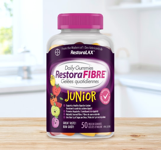 A clear bottle of RestoraFIBRE® Junior Daily Gummies with a pink cap and a purple label featuring cartoon fruit characters and